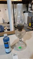 Full view of the vintage glass oil lamp with chimney alongside the bottle of lamp oil.