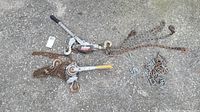 Two one-ton lever chain winches with attached chains lying on ground, showing wear and rust.