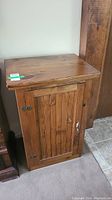 Wooden cabinet with vertical slat front door, showing top and front. Cabinet door has metal hinges and handle.
