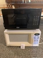 Two microwaves stacked: black Master Chef on top and white Sanyo below, showing front panels and keypad controls.