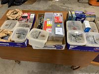 Three cardboard flats containing multiple plastic containers and boxes filled with various nails and screws.