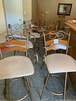 Seven bar height bar stools grouped together showing metal frames and tapestry seats. Visibly worn upholstery and wood slats on backs.