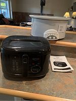 Photo showing black Betty Crocker deep fryer with dial control and manual beside a white Crock-Pot slow cooker