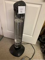 Full view of the EnerG+ oscillating space heater standing on a concrete floor in front of a white door, showing its protective grille and round base.