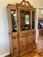 Front view of hardwood china cabinet showing three glass doors on upper section with wood scroll decor, three drawers in middle with round handles, and three cabinet doors on lower section with burled wood appearance.