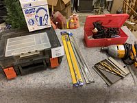 Two Black & Decker corded drills, various drill bits, red plastic case with soldering iron and solder, and boxed hearing protection ear muffs displayed on a workbench.