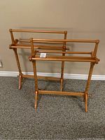 Two identical maple quilt or blanket stands displayed side by side on carpeted floor against a wall.