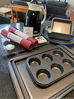 Baking pans, silicone mats rolled, cooling racks, Thermos jug, timer and thermometer arranged on table