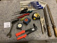 Overview of various hand tools laid on surface, including screwdrivers, chisels, files, measuring tapes, vice-grip, wrench, and crimper tool.
