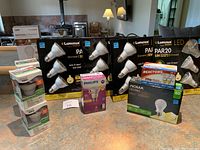 Photo showing various boxed and packaged light bulbs on a counter including Luminus Elite PAR20 50W dimmable LED bulbs, Noma LED bulb, halogen floodlights, and motion activated bulb.