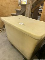 Closed view of large off-white plastic storage bin on caster wheels in a garage setting.