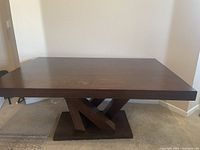 Full front view of the rectangular wooden dining table showcasing the dark cherry wood finish and geometric base design.