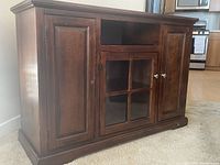 Photo of cherry wood TV cabinet showing two paneled side cupboards, a central glass-paned cabinet, and an open shelf at the top.