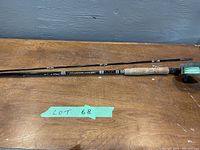 Partial view of the fiberglass rod with cork handle and reel, showing its length and detailing on the shaft with white accents.