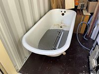 White clawfoot bathtub showing interior wear and rust spots, placed indoors on floor