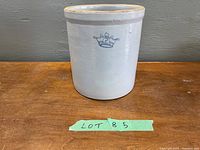 Front view of the antique crock showing the No 2 crown mark on the white glazed stoneware body sitting on a wooden surface.