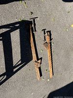 Two vintage wooden clamps laying on asphalt, showing side view with metal screw tightening components and long wooden bodies with notched adjustments.