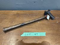Full view of the antique blacksmith swage hammer lying flat on a wooden surface showing the wooden handle and iron head with wear.