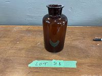 Front view of the brown glass vase on a wooden surface with lot tag visible.