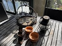 Photo of the cast iron candle holder with glass votive holders, the metal lantern with candle, three small copper candle holders, and two terracotta bowls on a wooden table.
