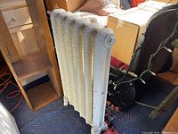 Side view of the Victorian cast iron radiator showing six embossed floral patterned columns and cream paint.