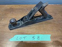 Front-side angle of the vintage metal hand plane showing the wooden front knob, metal body and rear wooden handle with repair.