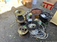 View of assorted electrical cables wound on metal and plastic spools and loose on ground.