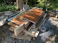 Overall view of the pile of building materials showing wood planks, metal rods, wire mesh and other supplies stacked outdoors on gravel.