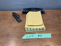 Desk with black I.B.F. Canada 3-hole punch, black stapler, and stack of yellow and green envelopes