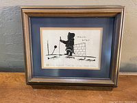 Frontal image of the framed original Inuit ink drawing depicting an Inuit man in traditional clothing with a spear and igloo-like structure, signed by Henri Napartuk.
