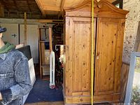 Full front view of a vintage pine armoire cabinet with curved top and two doors. Tape measure shows height approximately 85 inches.