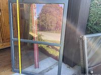 Gray metal framed storm window standing against outdoor wall, measuring tape shows vertical height around 40 inches.