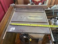 Top view of vintage metal table saw showing measuring tape for width around 23 inches and rusted surface with blade slot for saw blades.