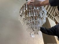 Ceiling light held by person showing tiers of elongated clear crystal prisms hanging from ornate metal base.