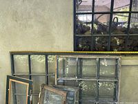 Full view of four vintage wooden windows arranged against a wall, showing multiple glass panes and distinct sizes.