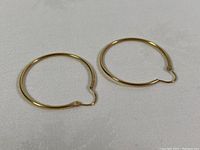 Pair of yellow gold hoop earrings on white cloth background, showing front view of hoops closed.