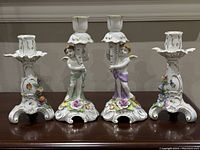 Photo showing both pairs of candleholders, two with cherubs holding candlesticks and two simpler floral decorated bases
