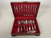 Full view of the cutlery sets displayed in the open wooden chest lined with red velvet, showing knives, forks, spoons and other utensils.