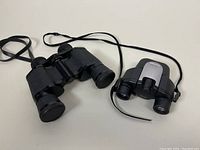 Two binoculars shown side by side on flat surface including the TRAQ 2001 and Pentax UCF-G.