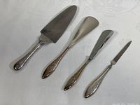 Full view of cake cutter, two shoe horns, and nail file laid out on white pattern cloth showing shape and size.