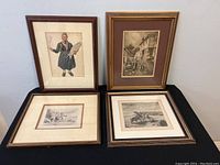 Four old framed etchings displayed on a black surface, featuring varied subjects including people and horses, showing overall condition and frame details.