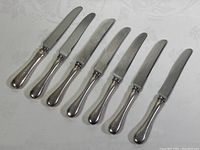 Seven 9-inch dinner knives arranged in a row, showing profile and blade shape, all with sterling silver handles.