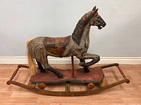 Side profile of the handcrafted wooden rocking horse showing paint detail, wooden base, and horse figure with a mane, tail, and saddle area.