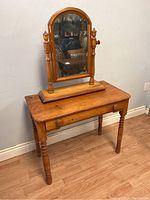 Photo showing top and front view of wooden desk with vanity mirror mounted on it, highlighting the aged surface and drawer knobs.