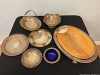 Photo of all items including the large oval silver plated serving tray with wooden cutting board insert, various silver plated plates and bowls including the footed condiment bowl with blue glass insert.