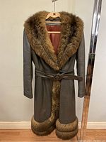 Full front view of brown leather coat with faux fur trim on large collar, front, and hem. Coat is belted and hanging on hanger.