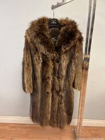 Full view of the vintage mid-length raccoon fur coat hanging on a rack, showing the overall length, texture, and colors of the fur.