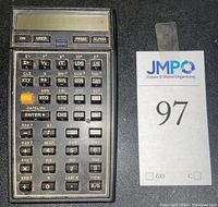 Front view of HP 41C scientific calculator showing alphanumeric display and function keypad with various scientific and programming keys. USB lot sticker placed beside it.