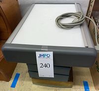 Color-Central light box with gray sides, white top surface, and attached electrical cord, wider view showing approximate size.