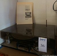 Oracle turntable under clear dust cover with instruction manual and paperwork standing behind